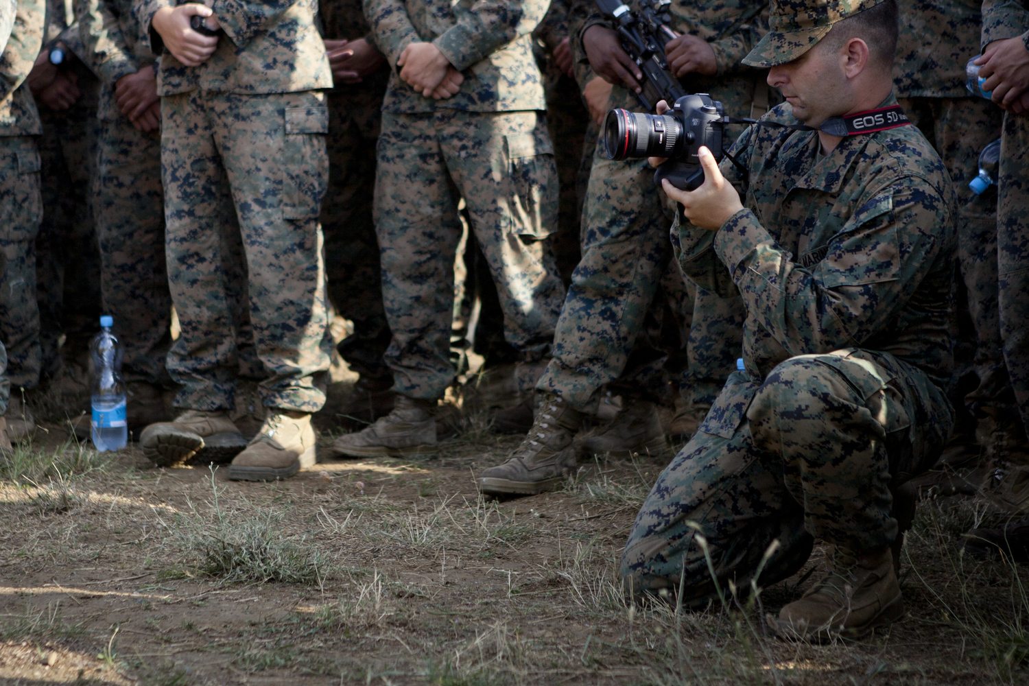 A Marine combat photographer kneeling with a DSLR, photographing a formation during a training exercise